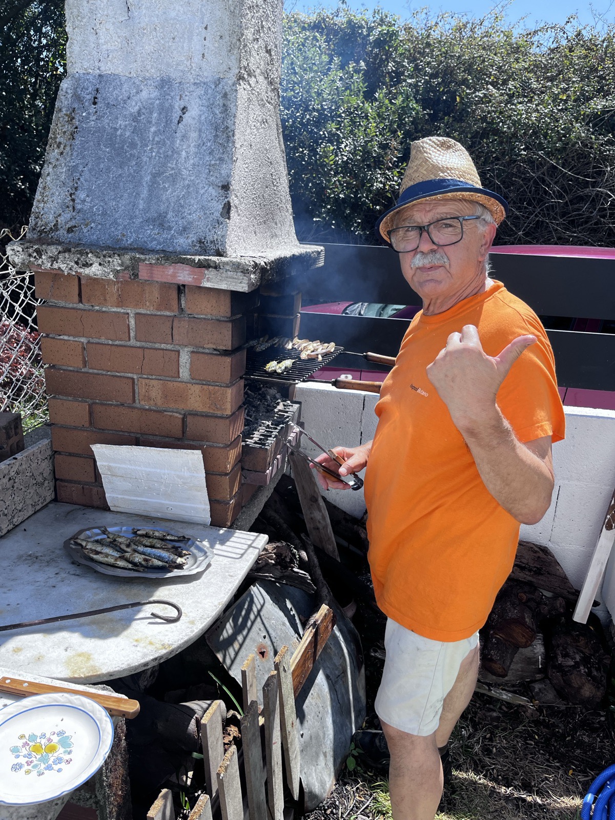 Dad in straw hat at the garden brick BBQ, sardines on the grill, smoke rising